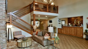 A spacious lobby with a wooden staircase, a reception desk, and a comfortable seating area with a sofa and armchairs. - GrandStay Hotel & Suites (Sisters)