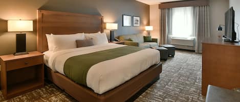 A hotel room with a large bed, a sofa, a desk, and a TV.