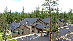 A hotel with a "NOW OPEN" sign, multiple parking spaces, and a building surrounded by trees. - GrandStay Hotel & Suites (Sisters)