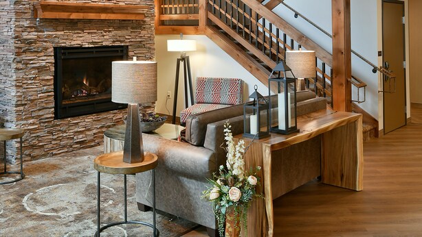 A spacious living area with a stone fireplace, a wooden staircase, and a large chandelier. - GrandStay Hotel & Suites (Sisters)