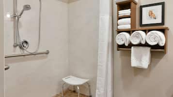 A bathroom with a shower, a small stool, a towel rack with towels, and a framed picture on the wall.