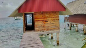 A wooden overwater bungalow with a red roof, a wooden door, and a wooden deck leading to the water. - Private Over the Water Cabin on San Blas Island (Las Huacas)