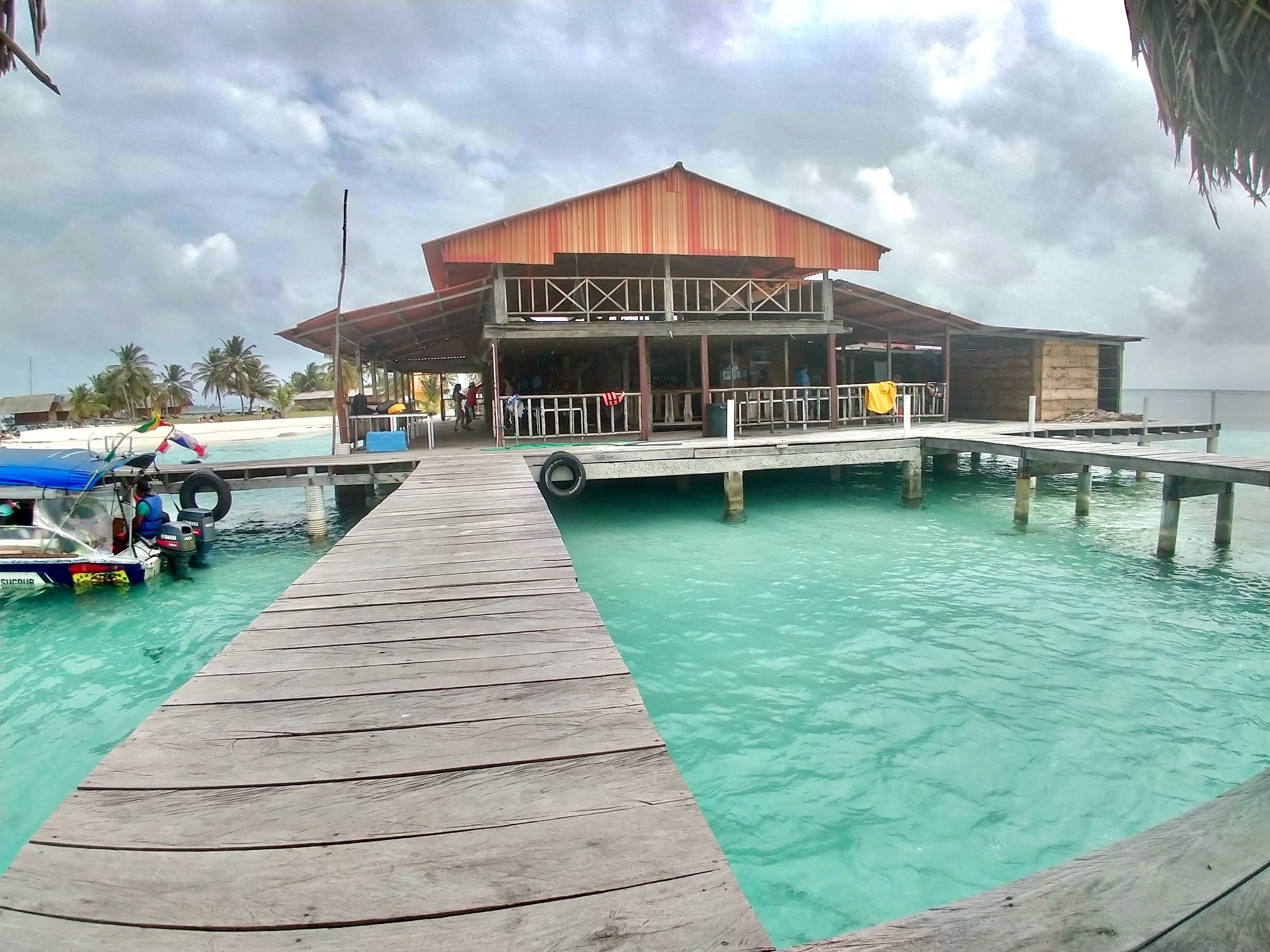 A wooden pier leading to a building with a covered area, situated over clear turquoise water.