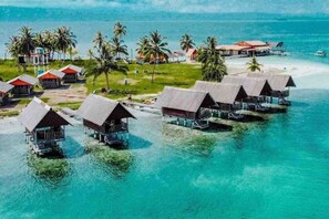 Des bungalows sur pilotis, dotés de toits de chaume, reliés par des passerelles et entourés d’une eau turquoise cristalline et de palmiers.