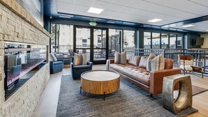 A modern lounge area with a stone wall, comfortable seating, a round wooden coffee table, and large windows offering views of the city. - 04505_p9 (Breckenridge)