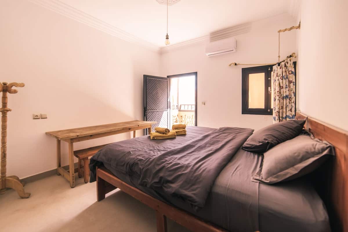Ein Schlafzimmer mit einem Holzbett, einer Bank, einem Kleiderschrank und einem Fenster mit Vorhängen.