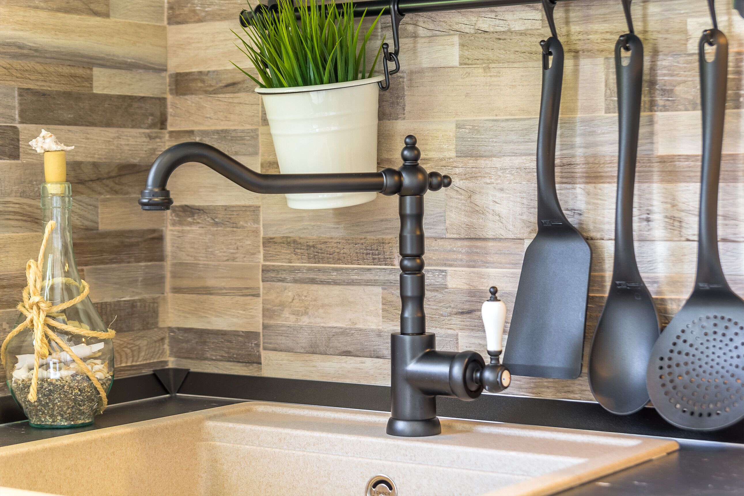 A kitchen with a modern faucet, a hanging pot of green plants, and kitchen utensils.