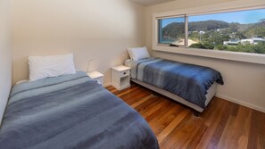 A bedroom with two beds, a nightstand, and a window with a view of a beach and hills.
