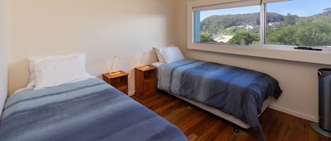 A bedroom with two beds, a window with a view of a beach and hills, and a radiator.