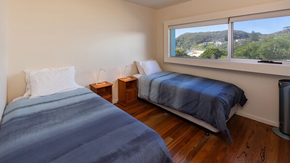 A bedroom with two beds, a window with a view of a beach and hills, and a radiator.