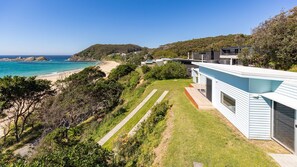 A coastal property with a modern house, a pathway leading to the beach, and a view of the ocean.