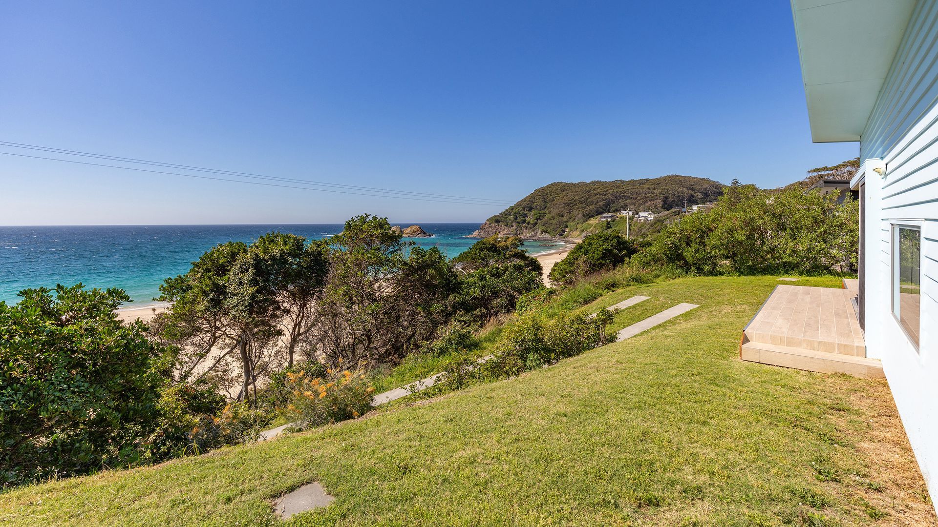 A coastal property with a grassy lawn, a pathway leading to a beach, and a view of the ocean.