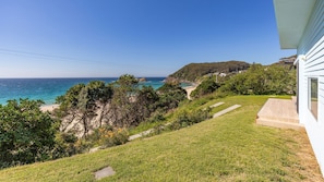 A coastal property with a grassy lawn, a pathway leading to a beach, and a view of the ocean.