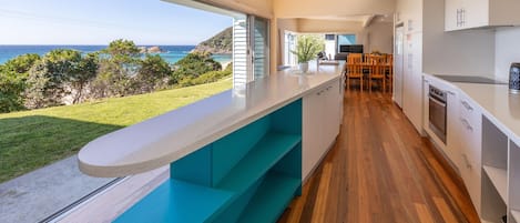 Una cocina moderna con vista al océano, suelo de madera y un comedor con sillas.