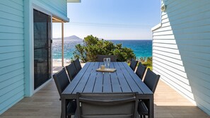 A wooden deck with a table and chairs, overlooking a coastal view.