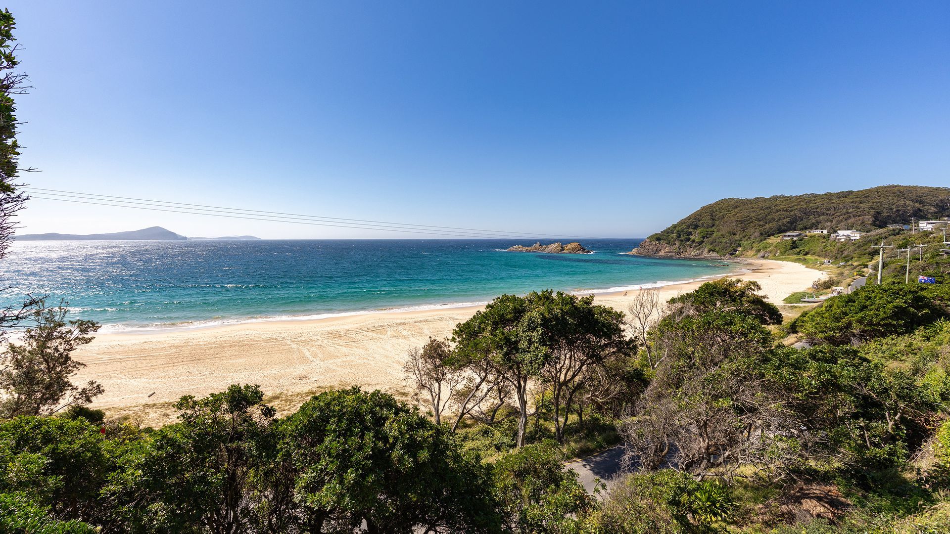 Eine Küstenlandschaft mit Strand, blauem Himmel und sanften Hügeln im Hintergrund.