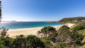 A coastal landscape with a beach, clear sky, and distant hills.