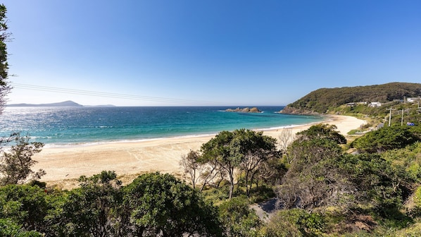 A coastal landscape with a beach, clear sky, and distant hills.