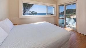 A bedroom with a large bed, a window, and a sliding glass door leading to a balcony.