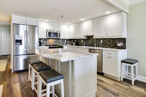 A modern kitchen with white cabinetry, stainless steel appliances, a central island with bar stools, and a herringbone tile backsplash.
