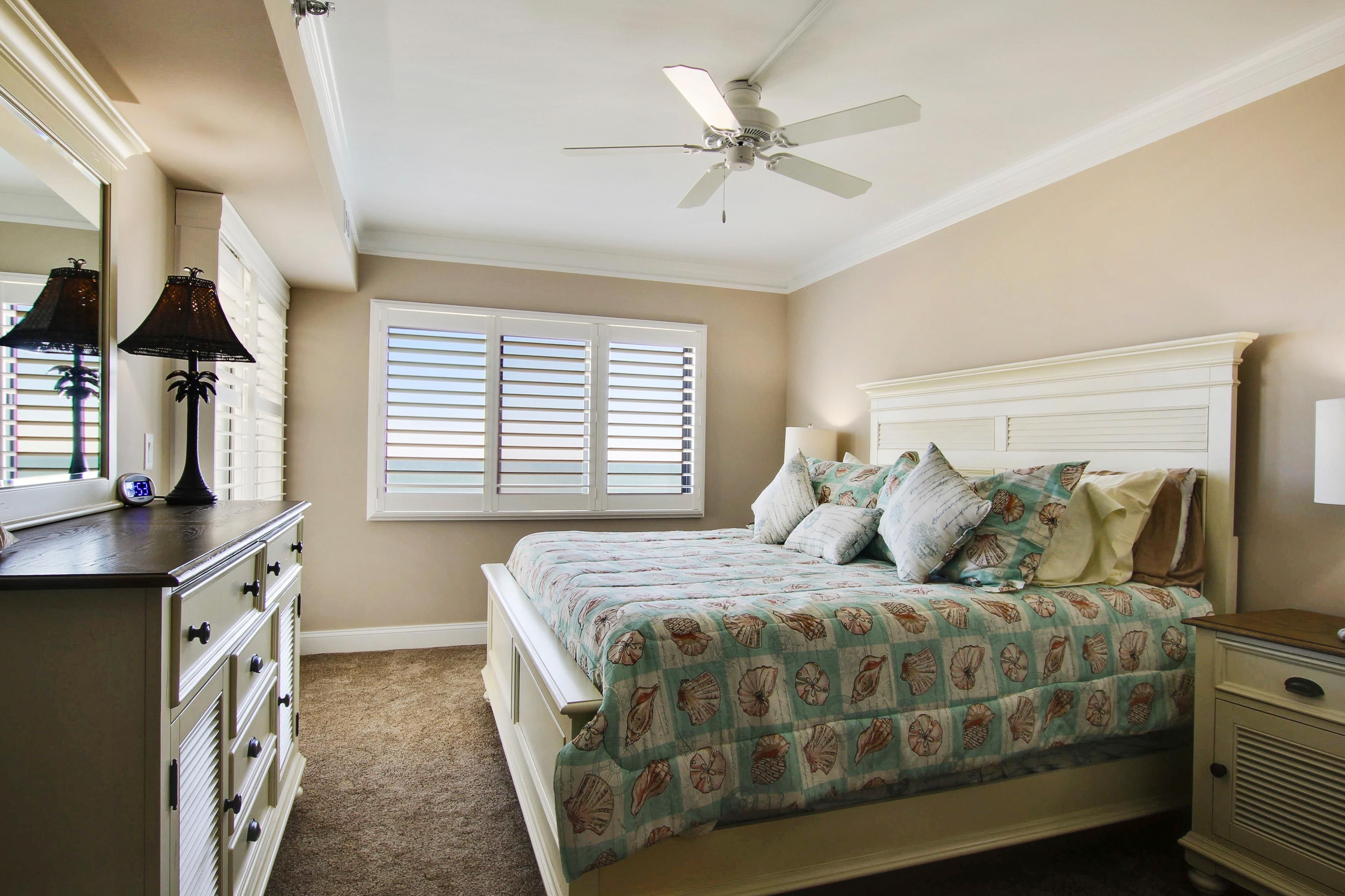 A bedroom with a bed, a nightstand, a dresser, a ceiling fan, and a window with blinds.
