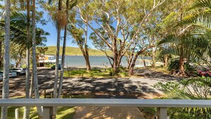 A lakeside view with a paved walkway, trees, and parked cars. - Reflections - Pacific Palms Holidays (Smiths Lake)