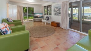 A spacious living area with green sofas, a woven rug, and a television. - Reflections - Pacific Palms Holidays (Smiths Lake)