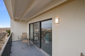 Ein Balkon mit Glastür, zwei Stühlen, einem kleinen Tisch und einer Lampe.