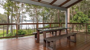 Eine Holzterrasse mit einem Glastisch und Bänken, mit Blick auf einen See und einen Wald.