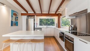 Cozinha moderna com uma ilha grande, eletrodomésticos de aço inoxidável e uma janela com vista para o verde.