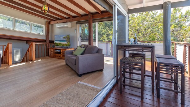 Uma sala de estar ampla com piso de madeira, um sofá cinza e uma mesa de madeira com duas cadeiras.