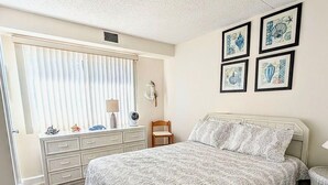 A bedroom with a bed, dresser, vanity, and artwork on the wall.