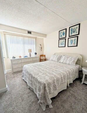 A bedroom with a bed, dresser, vanity, and artwork on the wall. - LINENS & DAILY ACTIVITIES INCLUDED*!!! THE CAPRI - 2BR/2BA condo with ocean & bay views. Indoor pool and many building amenties! (Ocean City)