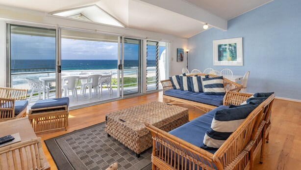 A spacious living area with a large sliding glass door leading to a balcony overlooking the ocean.