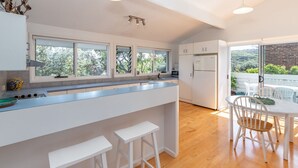 A modern kitchen with a large island, white cabinetry, and a view of a garden through the windows.