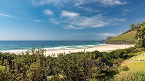 A beach with a clear view of the ocean and a grassy hillside. - Barefoot on Blueys - Blueys Beach (Blueys Beach)