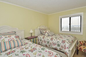 A bedroom with two beds, a nightstand, a lamp, and a window with blinds.