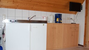 A compact kitchen with a white refrigerator, wooden cabinets, a coffee maker, and a mounted television. - Apartment morning sun (Pruchten)