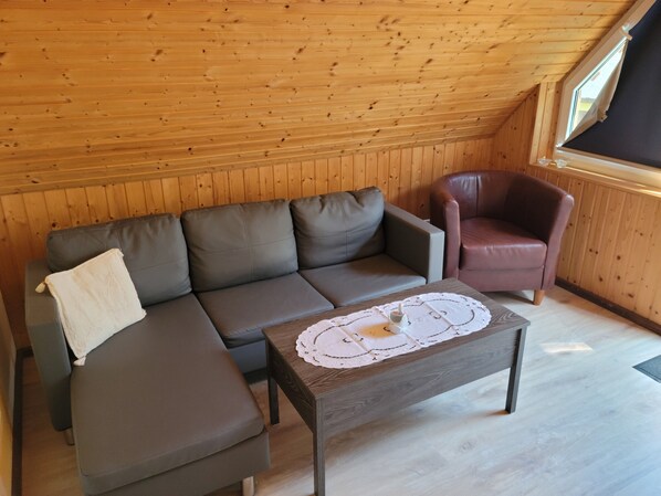A wooden-paneled room with a sofa, a chair, and a table with a doily.