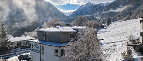 Un village de montagne enneigé, avec un bâtiment moderne portant l’inscription « APARTHOTEL DER GLETSCHERBUCK ».