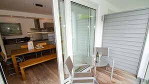 A modern kitchen with a dining area, a glass table with a bottle and glasses, and a sliding glass door leading to a balcony. - Apartment Glacier View 14.2 with balcony (Kaprun)