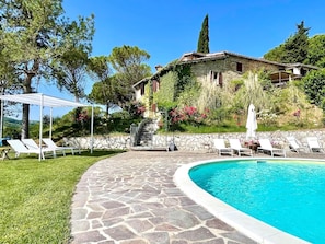 A stone-paved pool area with lounge chairs and a white pergola.