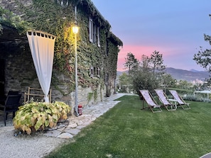 A stone building with ivy-covered walls, a stone pathway, a grassy lawn, and two lounge chairs.