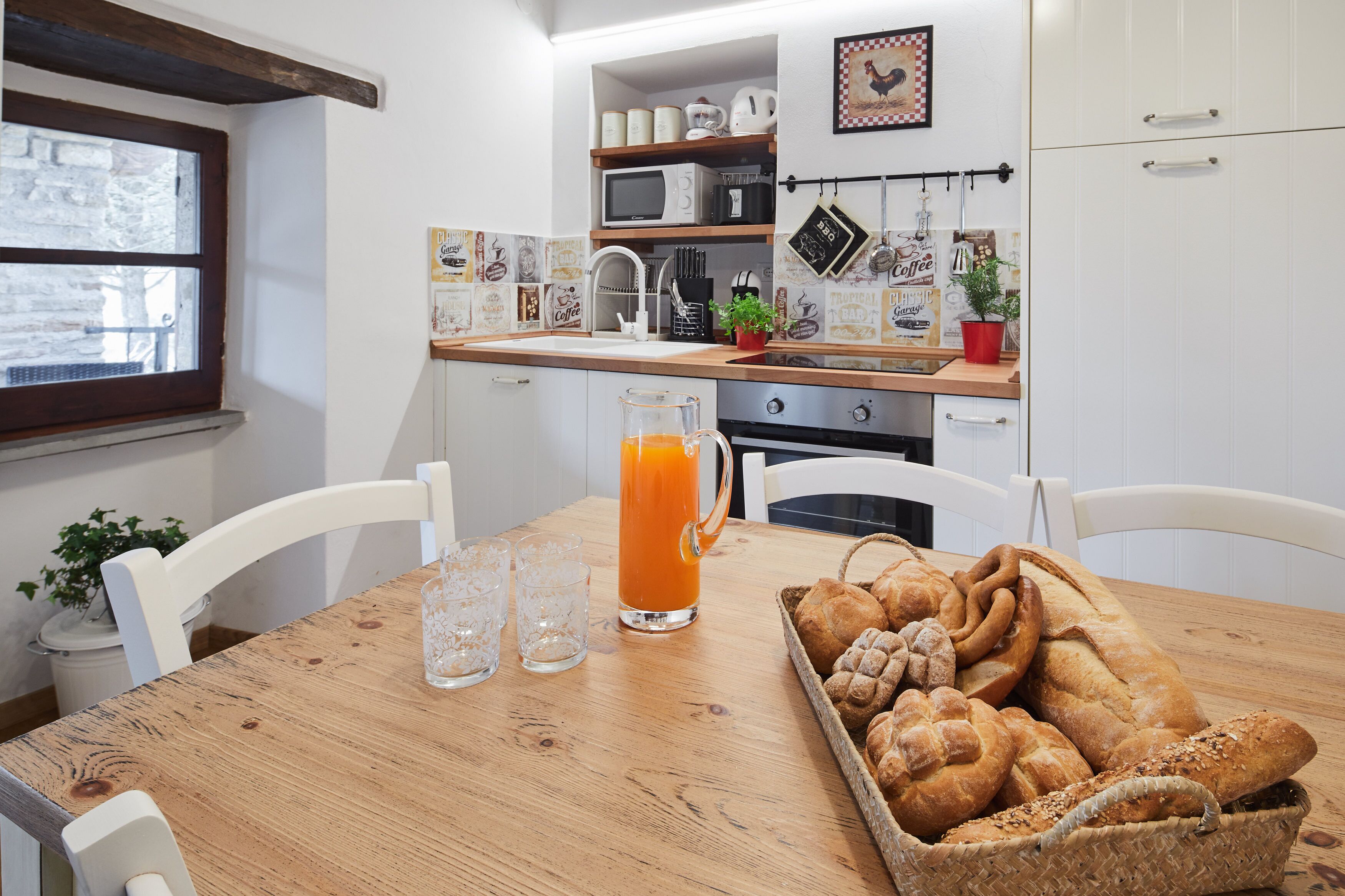 Une cuisine avec une table en bois, un panier de fruits et un verre de jus d’orange.