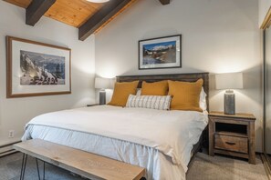 A bedroom with a wooden bed, two bedside tables, a bench, and framed pictures on the walls. - Mammoth Creek 36-Surround yourself by incredible mountain views! (Mammoth Lakes)