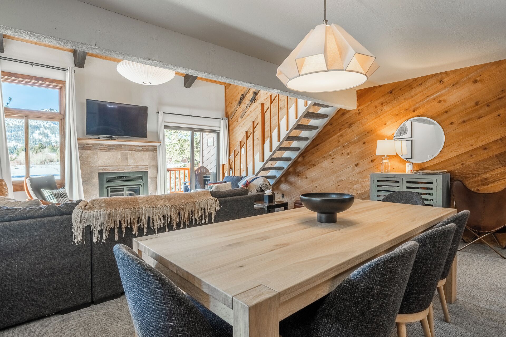 Ein gemütliches Wohnzimmer mit einer Holztreppe, einem Kamin und einem Essbereich mit großem Tisch und Stühlen.