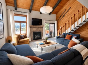 Ein modernes Wohnzimmer mit Kamin, einer großen Couch-Garnitur, einem Fernseher und einer Holztreppe.