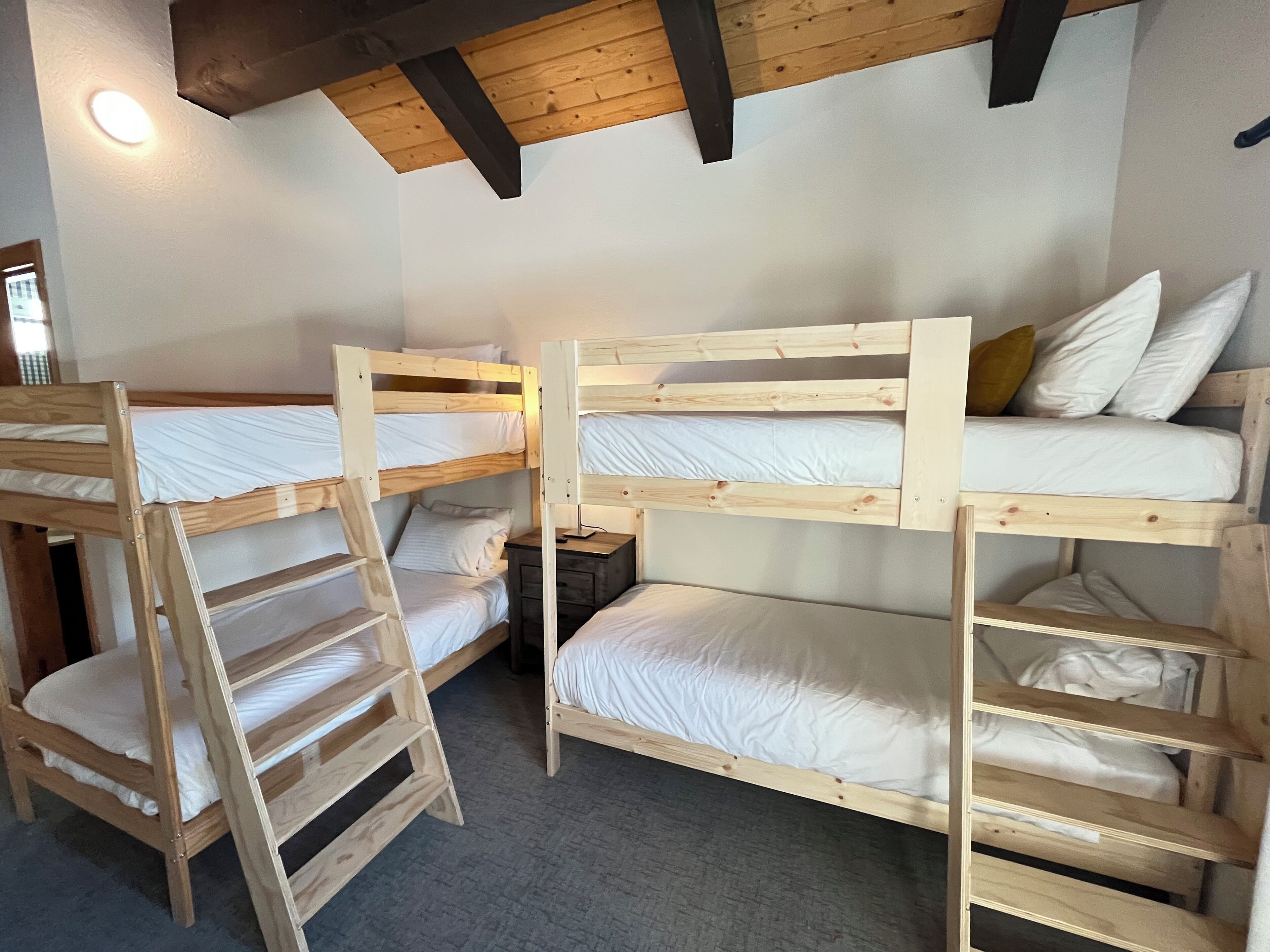 Een slaapzaal met stapelbedden, houten balken en een klein bureau.