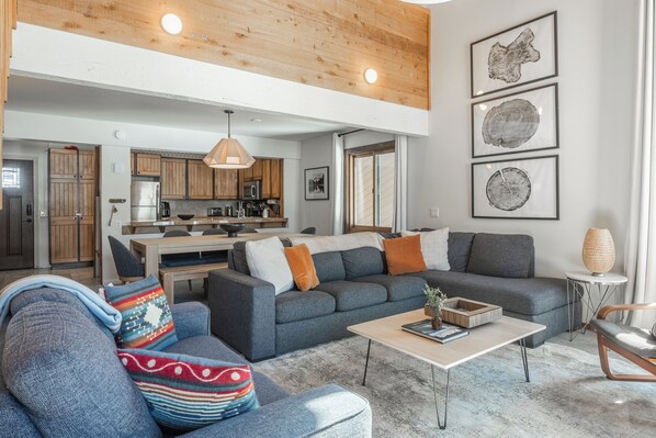 Un salón moderno con un sofá gris, una mesa de centro y una cocina al fondo.