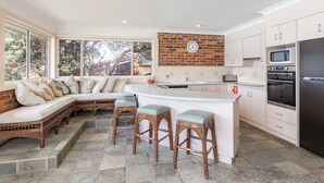 A kitchen with a built-in seating area, a brick backsplash, white cabinetry, and a stainless steel refrigerator.